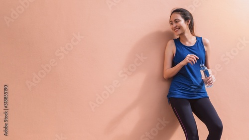 Fotografía Asian beautiful women holding water bottle after play yoga and exercise on orange wall background with copy space