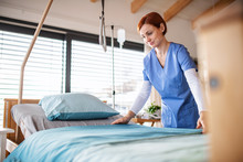Portrait Of Female Nurse Or Housekeeping Staff Changing Sheets In Hospital.