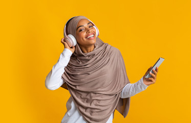 Wall Mural - Afro Muslim Girl Listening Music On Smartphone With Wireless Headphones