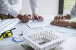 © Ngampol - Construction engineering or architect discussing a blueprint and building model while checking information on sketching meeting for architectural project in work site