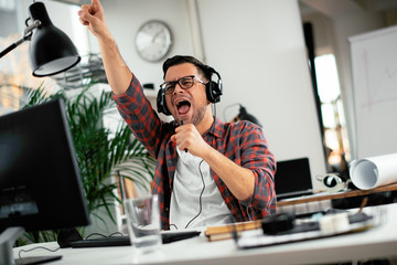 Attractive businessman in office. Young programmer with headphones singing at work. 