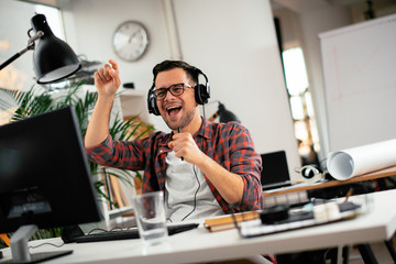 Attractive businessman in office. Young programmer with headphones singing at work. 