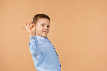 Wall Mural - cute little boy in shirt making Ok gesture on beige background.