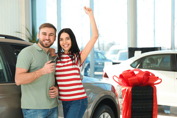 Happy couple with car key in modern auto dealership