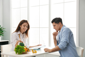 Wall Mural - Young nutritionist consulting patient at table in clinic