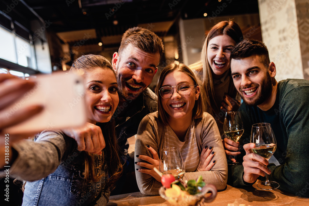 Group of young friends having fun in restaurant talking, laughing while dining at table and making selfie. - obrazy, fototapety, plakaty 