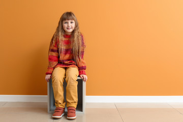 Sticker - Cute little girl in autumn clothes sitting near color wall