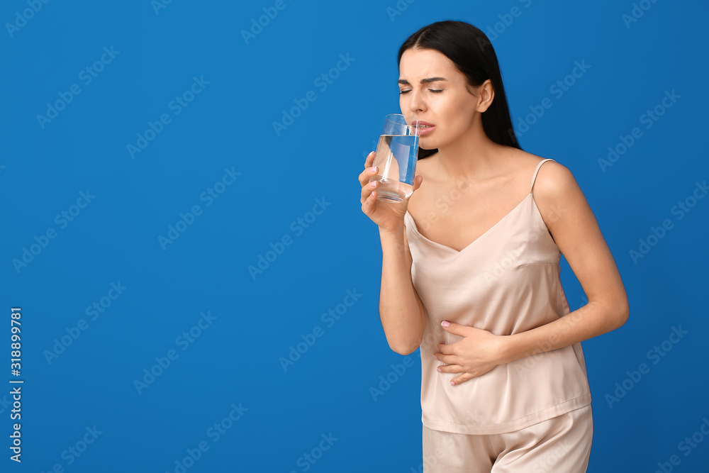 Beautiful young woman drinking water while suffering from stomachache on color background