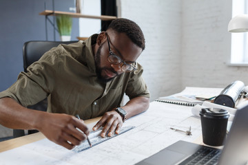 Afro-American architect working in office with blueprints.Engineer inspect architectural plan, sketching a construction project. Portrait of black handsome man sitting at workplace. Business concept.