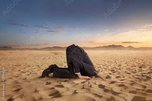 Fotografía Desparate businessman hiding head in the sand at the desert with copy space
