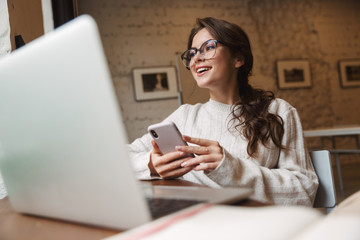 Poster - Image of young caucasian woman using laptop and smartphone in cafe