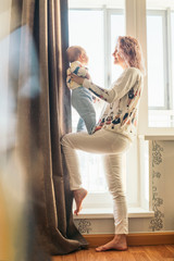 Wall Mural - Happy young mother with cute baby boy. At home near the window. Life style.