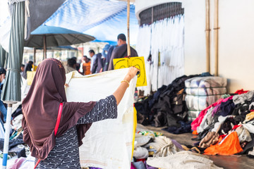 Thai woman is choosing used second hand clothes at flea market in Thailand