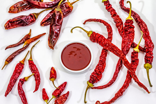 Spicy chili sauce in bowl isolated on white background. Different varieties of dry hot peppers, main ingredient for preparation. Cooking backdrop, mockup