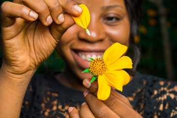 black girl holding a tree marigold sunflower pick the petals off one by one, close up