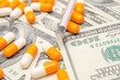 © yaroslav1986 - A lot of white and orange tablets on the background of dollar bills close-up. Concept of insurance, medicine, macro