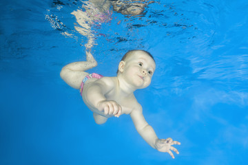 Little girl learns to swims underwater. Baby swimming underwater in the pool on a blue water background. Healthy family lifestyle and children water sports activity.