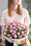 Fototapeta  - Young beautiful woman holding a spring bouquet of yellow tulips in her hand. Bunch of fresh cut spring flowers in female hands