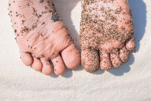 Closeup View Of Little Kids Cute Bare Feet Isolated On White Beach Towel Background Laying On Chair. Wet Healthy Skin Of Baby Dirty From Small Pebbles And Sand Of Tropical Seashore.