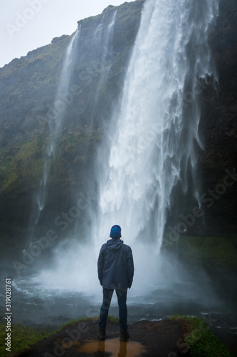 Fotografía Young traveling man looking up at the massive Seljalandsfoss waterfall near the ring road on Iceland's south coast