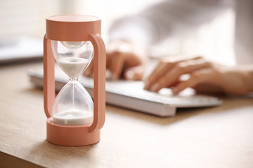 Hourglass and woman working on computer at table in office