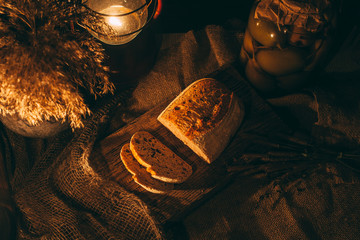 Pieces of sliced ​​freshly baked bread in the light of candles. Bread on a wooden board.Rural cozy surroundings.