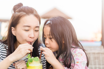 Wall Mural - Happy laughing little girl and her beautiful young mother drinking fresh pineapple smoothie together in restaurant.Summer smoothie drink concept.