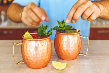 Barman is decorating Moscow mule cocktails in metallic cups with lemon and mint. Party concept.