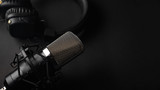 Fototapeta Miasto - Studio black studio microphone with studio headphones on a black background. Banner. Radio, work with sound, podcasts.