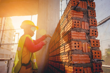 Bricklayer construction worker installing red brick masonry on exterior wall at outdoors construction site