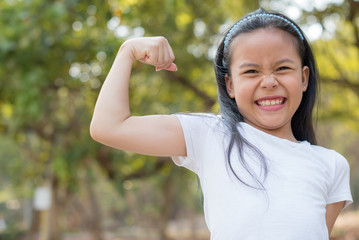 happy little asian girl child standing showing front teeth with big smile. showing arms muscles smil