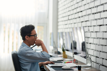 Wall Mural - office routine. side view of a young asian graphic designer in eyeglasses yawning while sitting at h