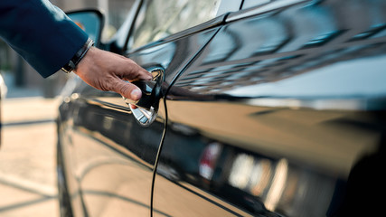 Cropped photo of a male hand opening the door of a black car while standing outdoors