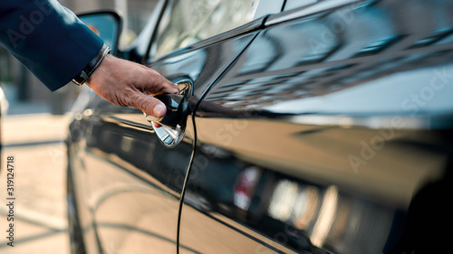 Photographie Cropped photo of a male hand opening the door of a black car while standing outd