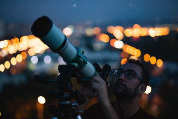 Wall Mural - astronomer with a telescope watching at the stars and moon with blurred city lights in the backgroun