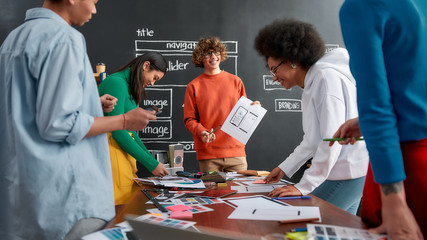 Wall Mural - responsive web design. young cheerful designer is showing some sketches to his colleagues while havi