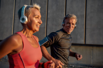 Wall Mural - Be healthy. Sporty and happy middle-aged couple in headphones running together through the city street in the morning