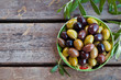 Assortment of fresh olives on a plate with olive tree brunches. Wooden background. Top view. Copy space.