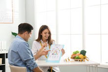Young Nutritionist Consulting Patient At Table In Clinic