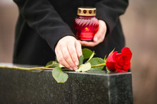 Woman With Candle Near Black Granite Tombstone Outdoors, Focus On Red Rose. Funeral Ceremony