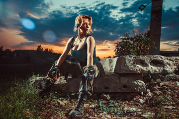 Sexy woman soldier with pistol is having a rest. Sunset on the background.