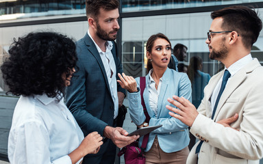 Coworkers standing outside in front of office buildings discuss about business plan.