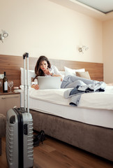 Young businesswoman working from hotel room on business trip, woman lying on the bed and using laptop.