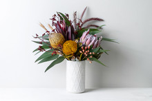 Beautiful Floral Arrangement Of Mostly Australian Native Flowers In A Vase, Including Protea, Banksia, Kangaroo Paw Eucalyptus Leaves And Gum Nuts On A White Table With A White Background.