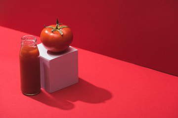 Wall Mural - fresh vegetable juice in glass bottle and ripe tomato on cube on red background