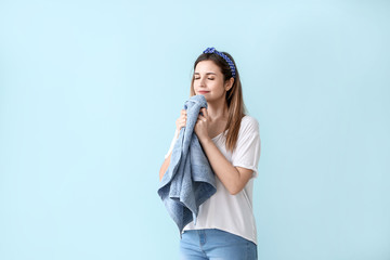 Beautiful young woman with clean towel after laundry on color background