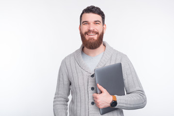 Happy bearded man in sweater holding laptop and looking confident at the camera