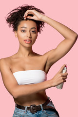 Wall Mural - attractive african american girl using spray deodorant, isolated on pink