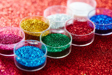 Multicolored Bright Shimmering Sparkles In Jars For Creative Crafts And Nails Art On Colorful Shining Red Background Close Up