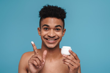 Wall Mural - Photo of shirtless african american man smiling and applying face cream